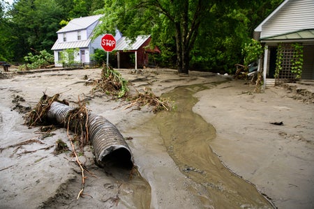 A thick layer of mud, debris, and receding flood water surround homes and cover a road intersection with a stop sign in Vermont